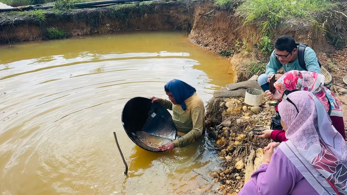 A miner panning for diamonds waist-deep in a muddy pool, Cempaka fields, Borneo
